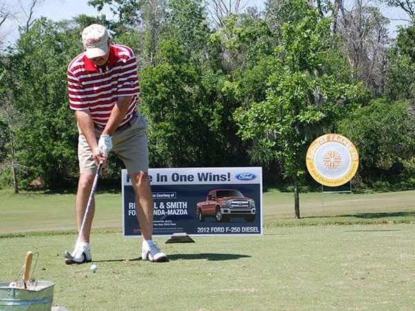 Golfer teeing off beside a Hole In One contest banner